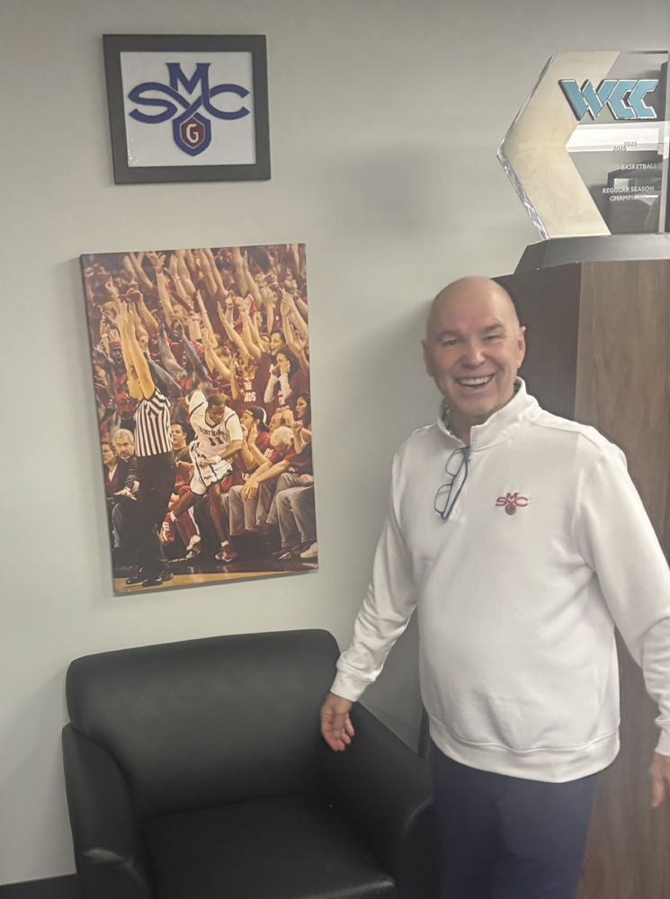 Randy Bennett in front of a photo celebrating his first win over Gonzaga.